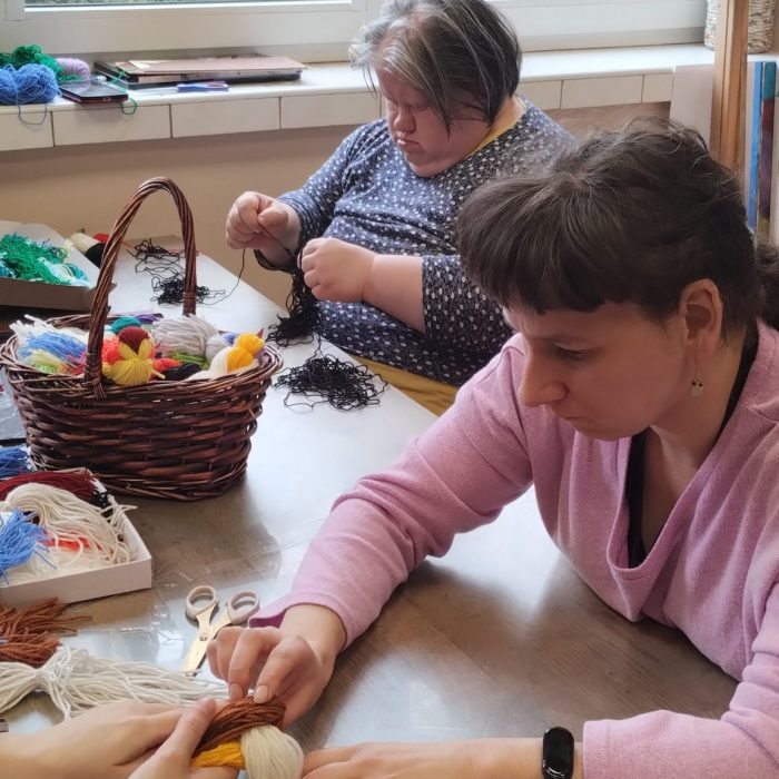 Dwie uczestniczki przygotowują kolorowe kartki i dekoracje podczas zajęć kreatywnych.