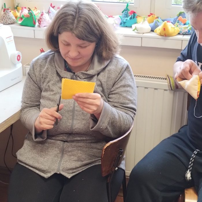 Uczestnicy wykonują ozdoby wielkanocne przy wspólnym stole podczas zajęć rękodzielniczych.