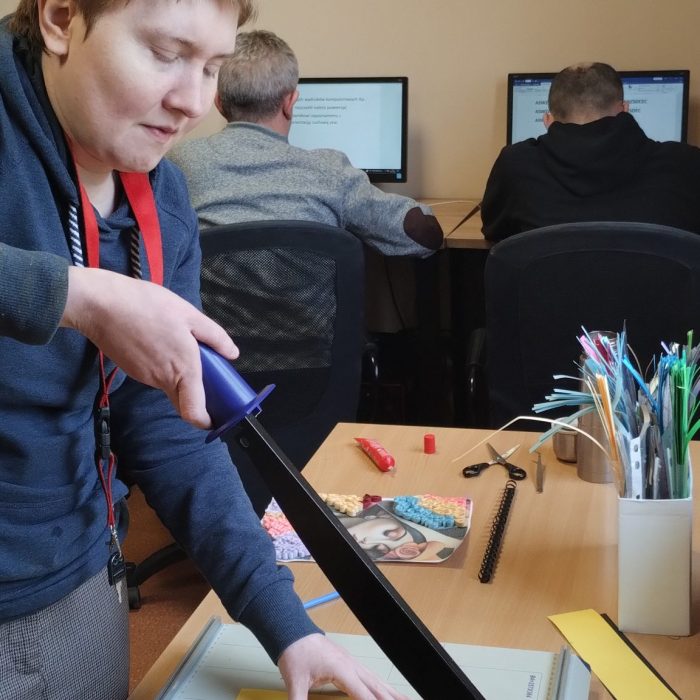 Uczestniczka zajęć rękodzielniczych ozdabia świąteczną dekorację przy stanowisku pracy.